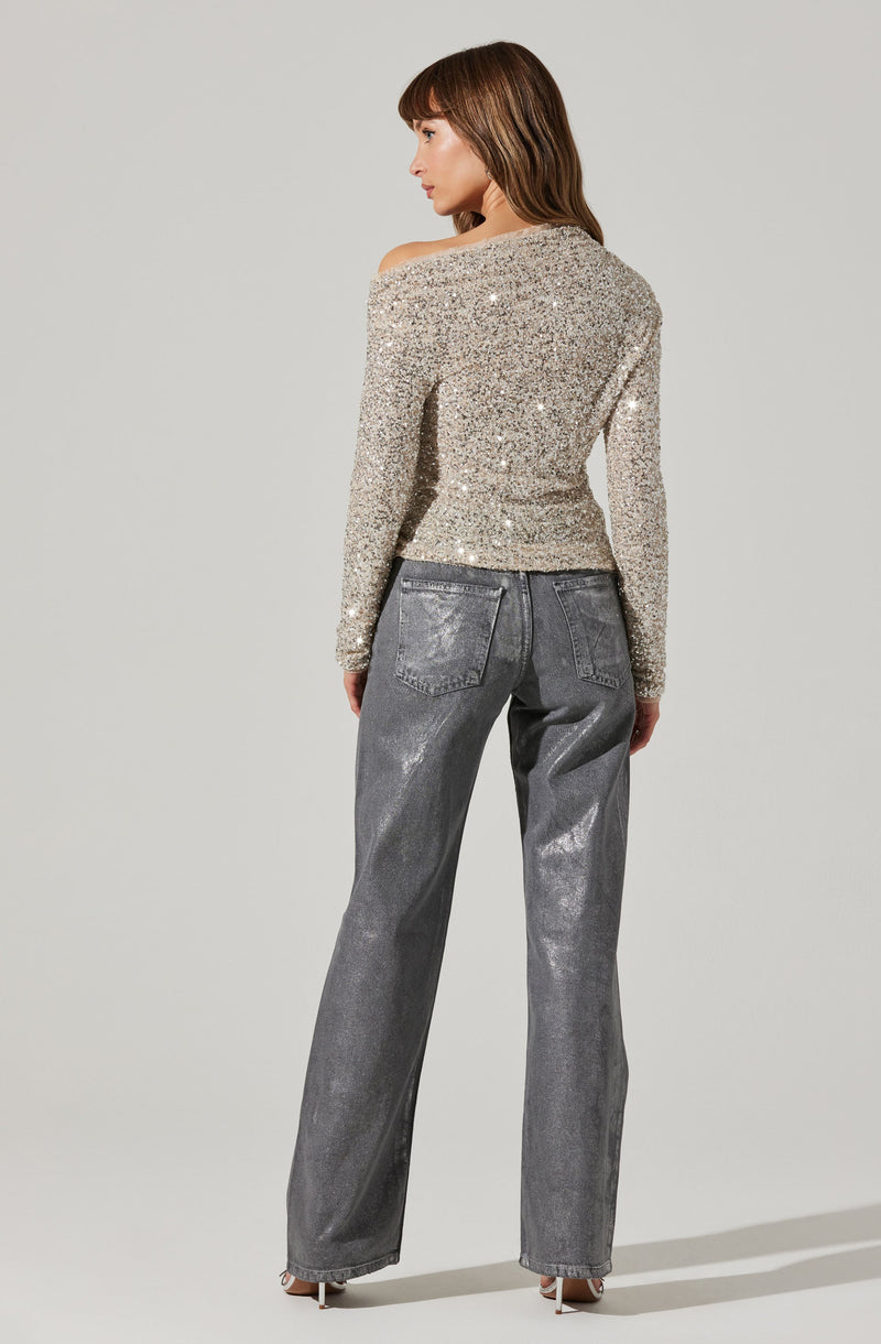 A woman is wearing a long-sleeve, off-the-shoulder top covered in silver sequins, paired with high-waisted, loose-fitting gray pants with a metallic sheen.