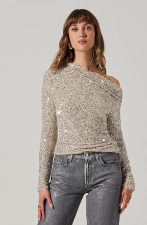 A woman is wearing a long-sleeved, off-the-shoulder top covered in silver glitter, giving it a sparkly and glamorous appearance. She pairs it with high-waisted, metallic gray jeans.
