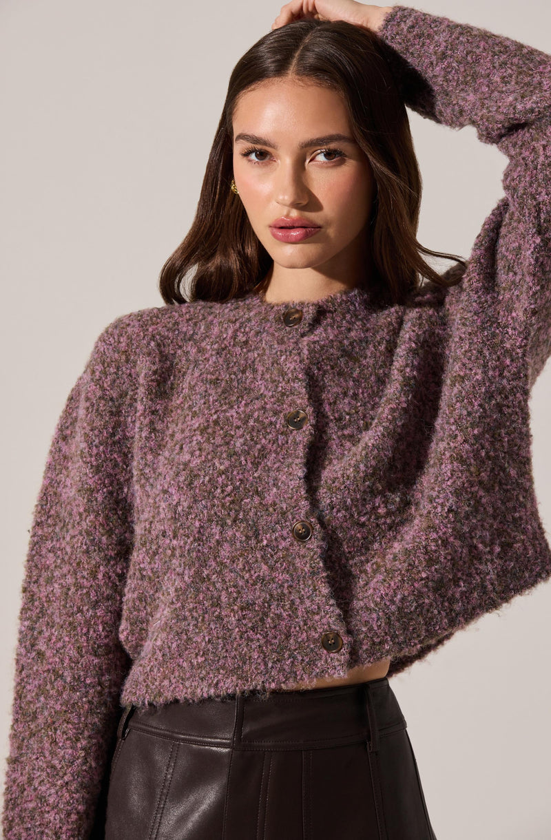 A young woman is wearing a cropped, button-up sweater with a textured, speckled pattern in shades of purple, pink, and gray.