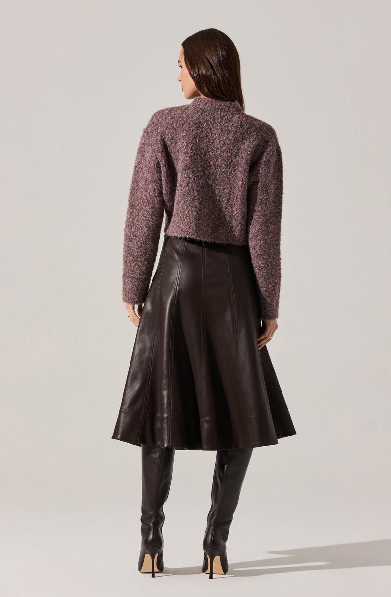 A woman is wearing a textured, long-sleeved, purple and gray knit sweater paired with a high-waisted, midi-length leather skirt that flares out. She completes the outfit with tall, black leather over-the-knee boots with stiletto heels.