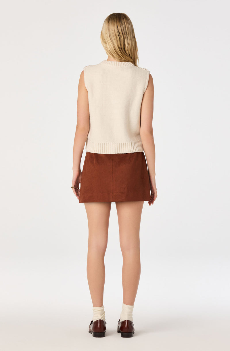 Woman wearing a sleeveless cream knit vest, a brown skirt, cream socks, and brown shoes.