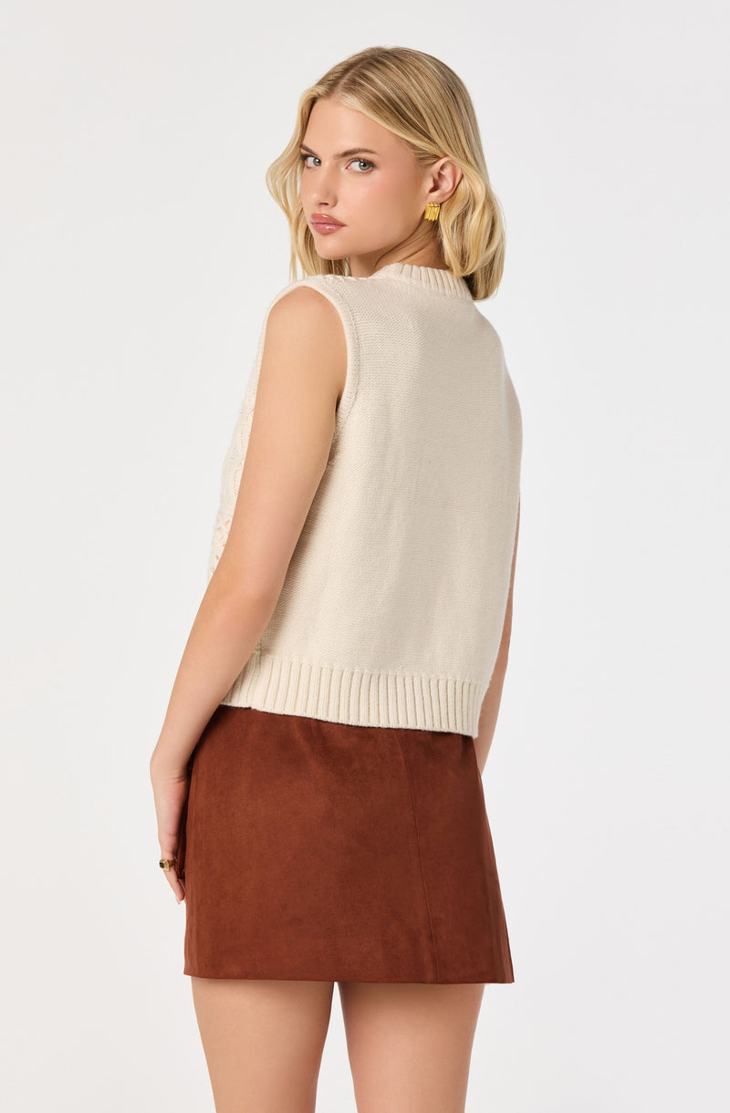 Woman wearing a sleeveless beige knit vest and a brown suede skirt.