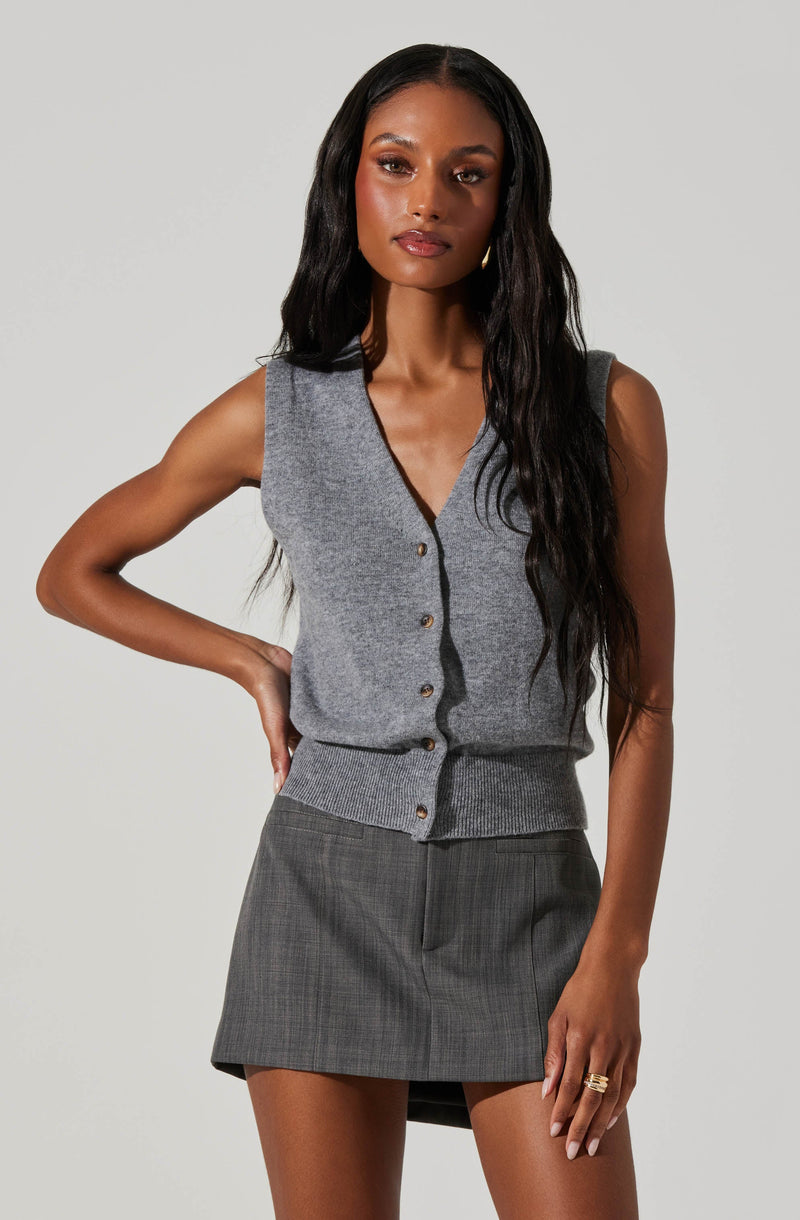 A woman is wearing a sleeveless, button-up gray vest with a V-neckline and ribbed hem, paired with a gray plaid mini skirt.