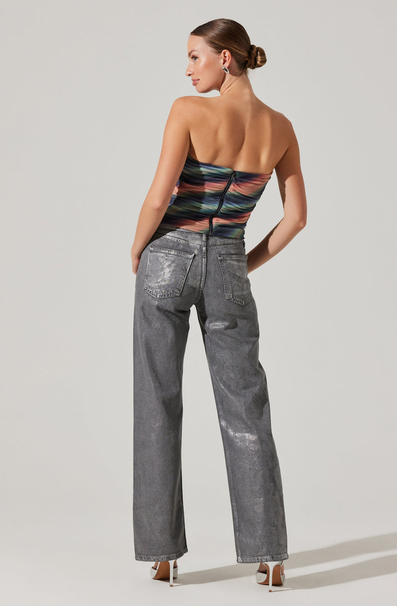 A woman is wearing a strapless, fitted top with horizontal stripes in various colors, including black, pink, green, blue, and orange. The top is secured with a black zipper at the back. She pairs this with high-waisted, loose-fitting, gray washed-out jeans that have a slightly distressed look and prominent back pockets. She is also wearing white high-heeled shoes.