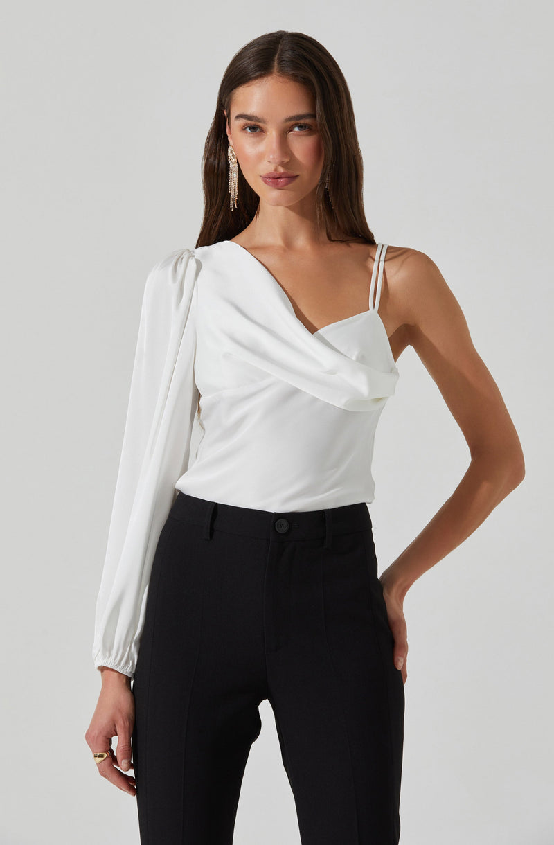 A woman is wearing a stylish white sleeveless top with thin spaghetti straps and a draped neckline. The top features a unique design with a long sleeve on her left arm that is gathered at the wrist, while the right side is sleeveless. She pairs it with high-waisted black trousers. She has long, dark hair and is accessorized with dangling earrings.