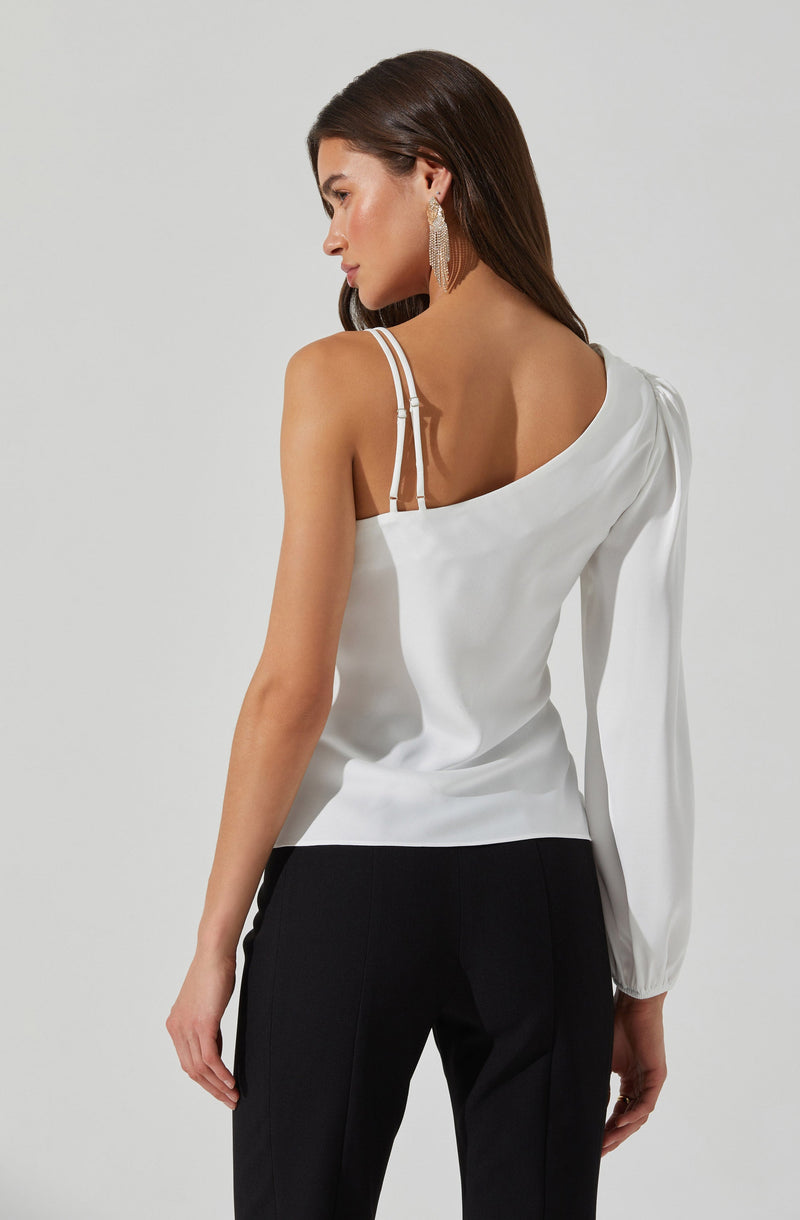 A woman is wearing a white satin top with thin, double straps on her left shoulder and a single strap on her right shoulder. The top has a draped, asymmetrical design with one long sleeve on the right side, while the left shoulder is exposed. She pairs it with black tailored trousers. She has long, dark hair and is accessorized with large, dangling earrings.