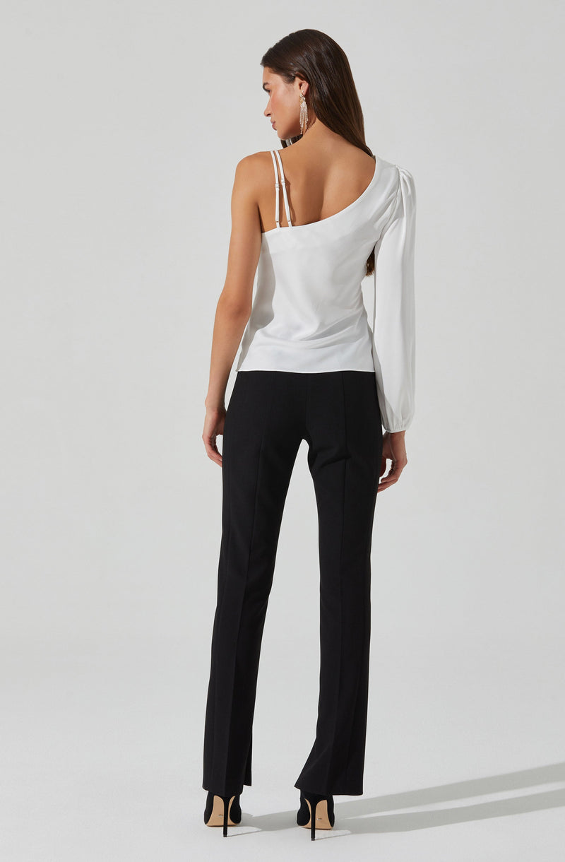 A woman is wearing a white satin top with spaghetti straps on her left shoulder and a long, flowing sleeve on her right arm. She pairs it with black tailored trousers that have a straight-leg fit. She is also wearing black high heels with ankle straps.