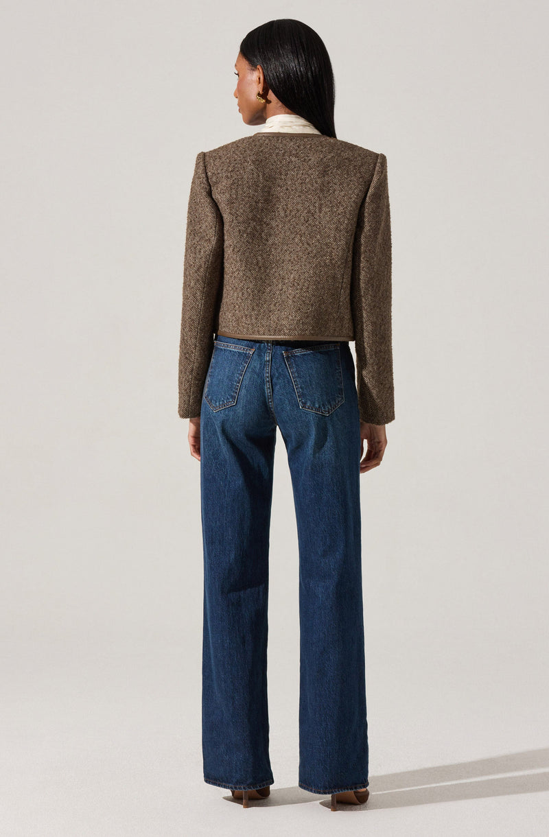 A woman is wearing a beige, textured, cropped blazer with long sleeves over a white collared shirt. She pairs this with high-waisted, straight-leg blue jeans.