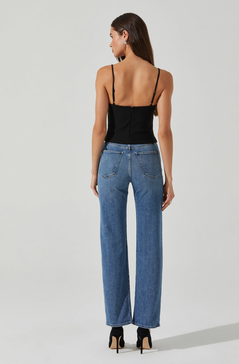 A woman is wearing a black sleeveless top with thin spaghetti straps, fitted at the waist, and high-waisted blue jeans with a straight-leg cut. She is also wearing black high-heeled shoes.