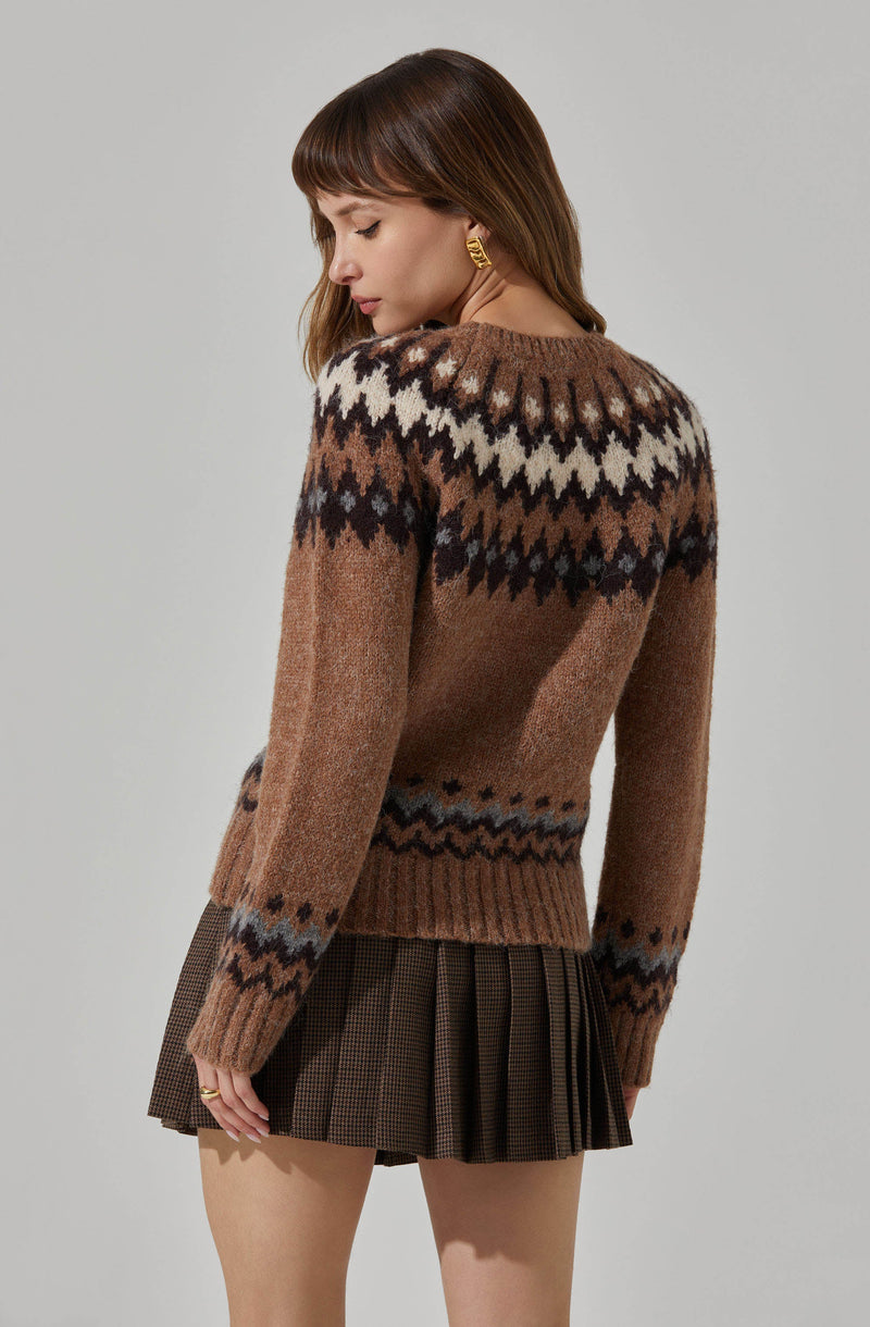 The woman is wearing a brown sweater with a patterned design featuring white, black, and gray geometric shapes across the shoulders and upper chest. She is also wearing a pleated skirt with a checkered pattern in shades of brown.