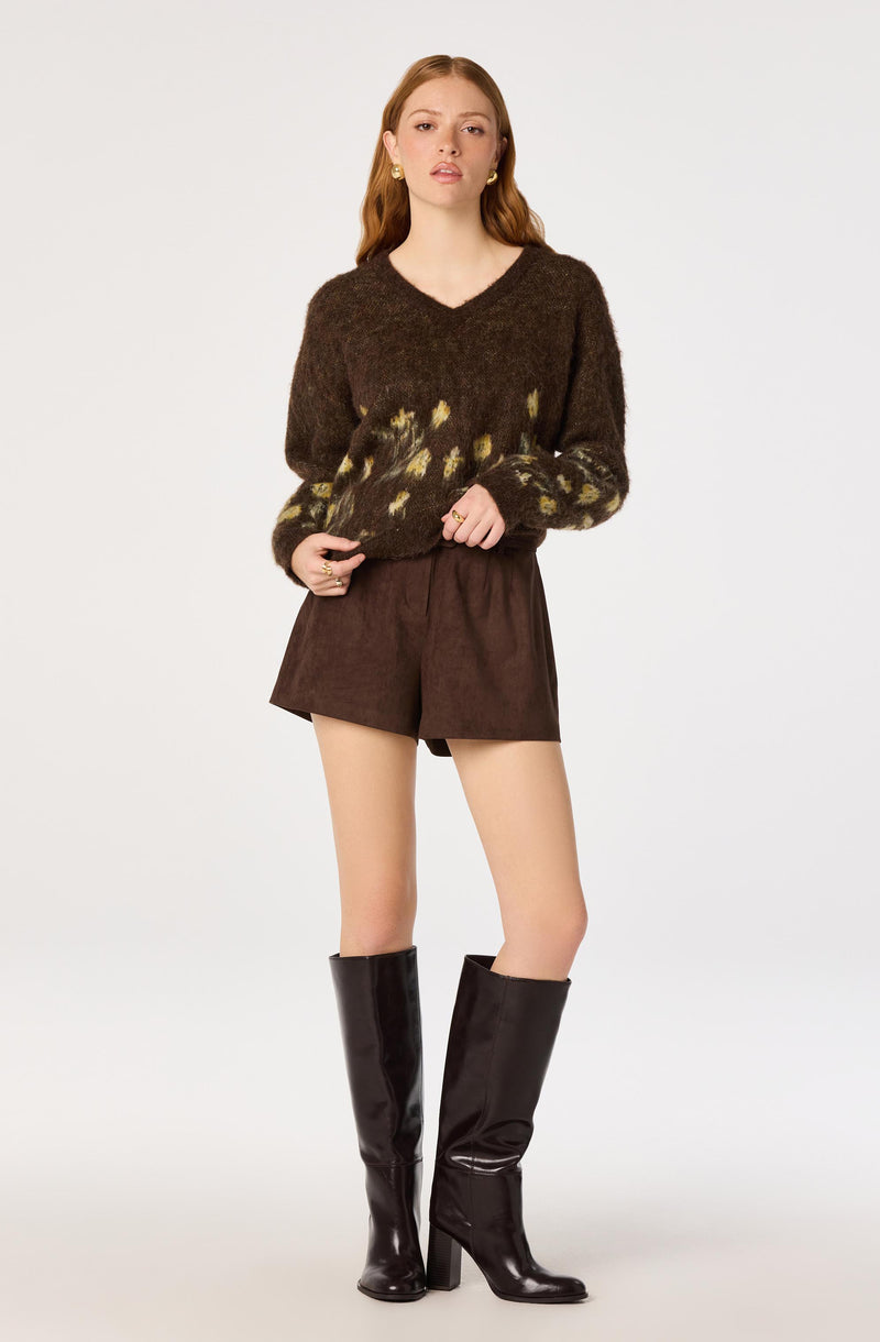 Brown fuzzy sweater with yellow and brown pattern, paired with brown shorts and tall black boots.