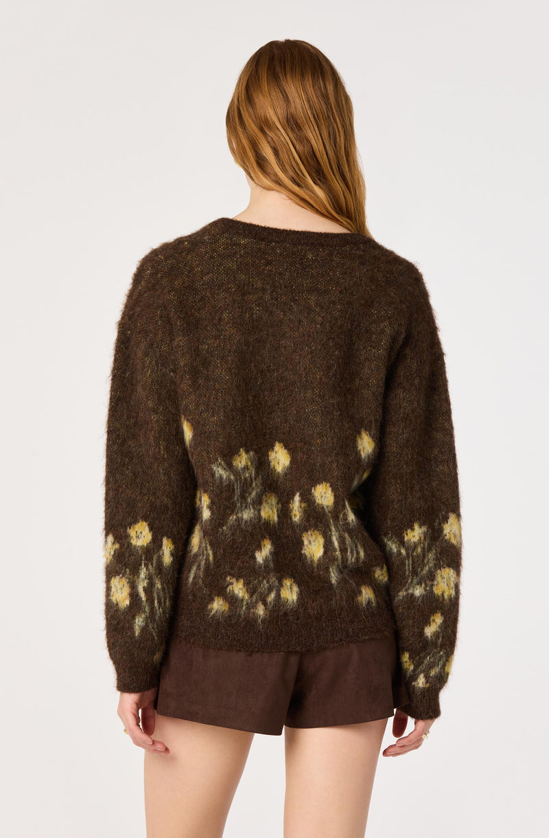 Back view of a woman wearing a brown fuzzy sweater with yellow floral patterns and brown shorts.