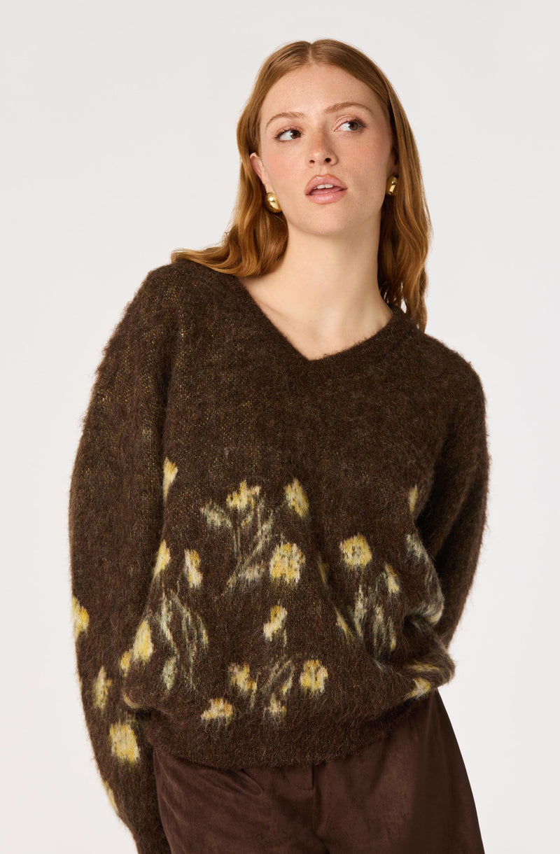 Woman wearing a dark brown knit sweater with yellow and beige floral patterns.