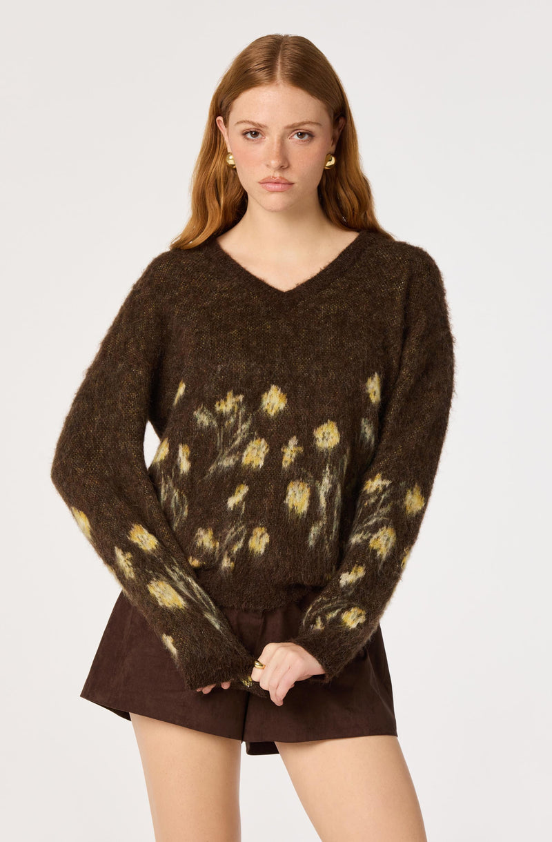 Woman in a brown sweater with yellow floral patterns and dark brown shorts.