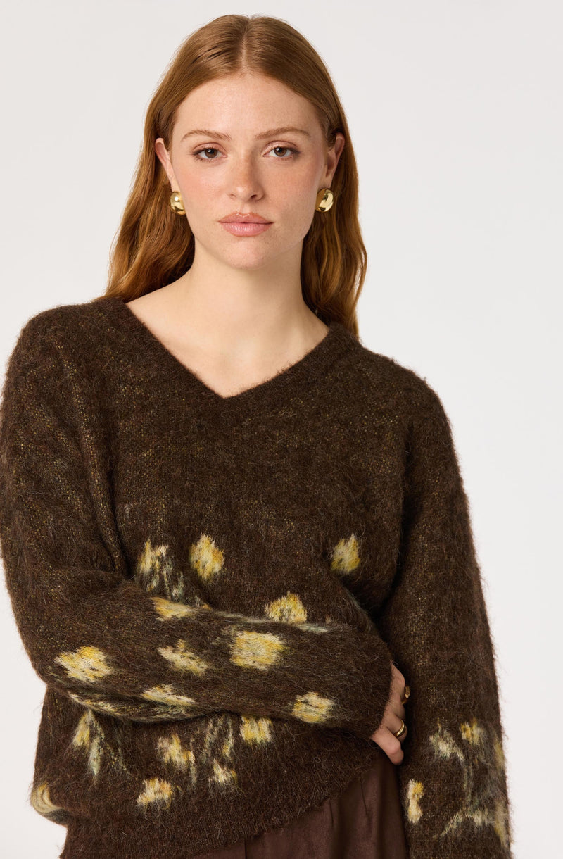 Woman wearing a brown fuzzy sweater with yellow and white flower-like patterns.