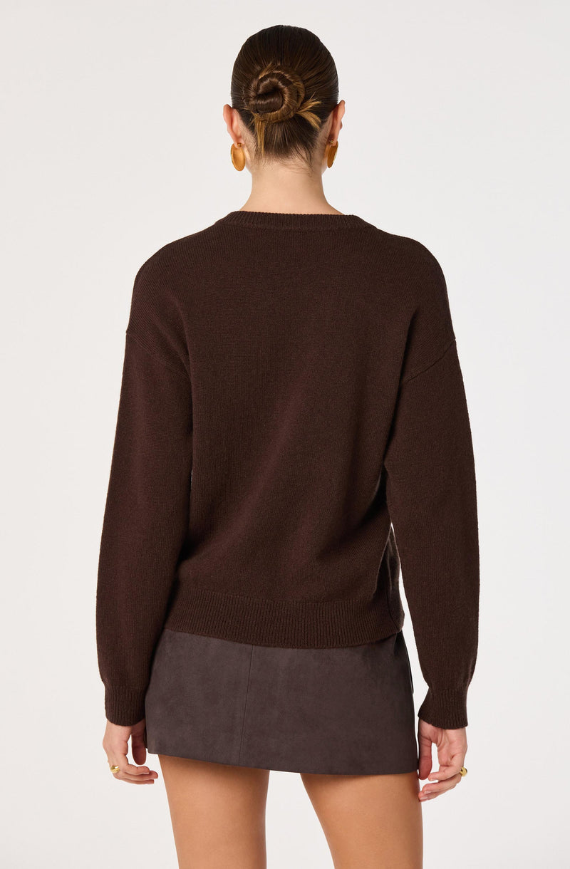 Woman wears a dark brown oversized sweater and a gray mini skirt, with her hair in a bun.