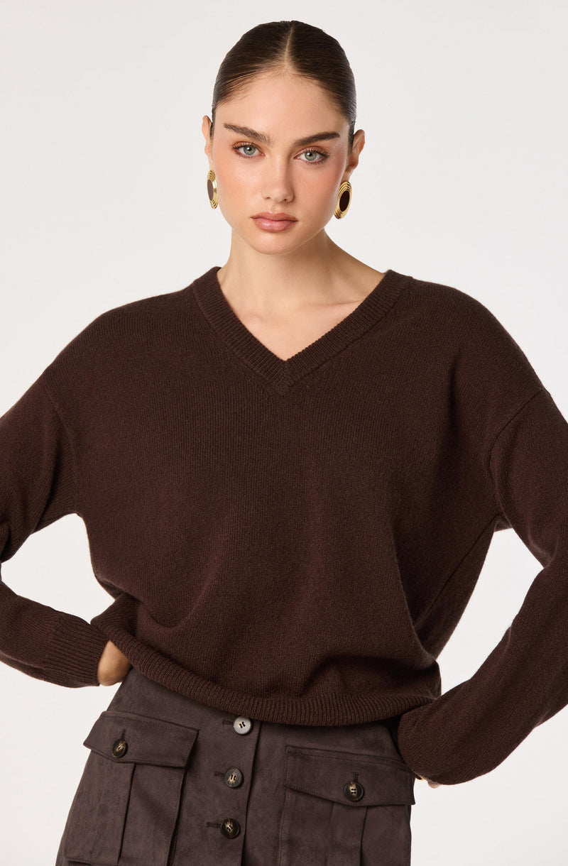 Woman wearing a dark brown v-neck sweater and high-waisted brown pants with buttons.