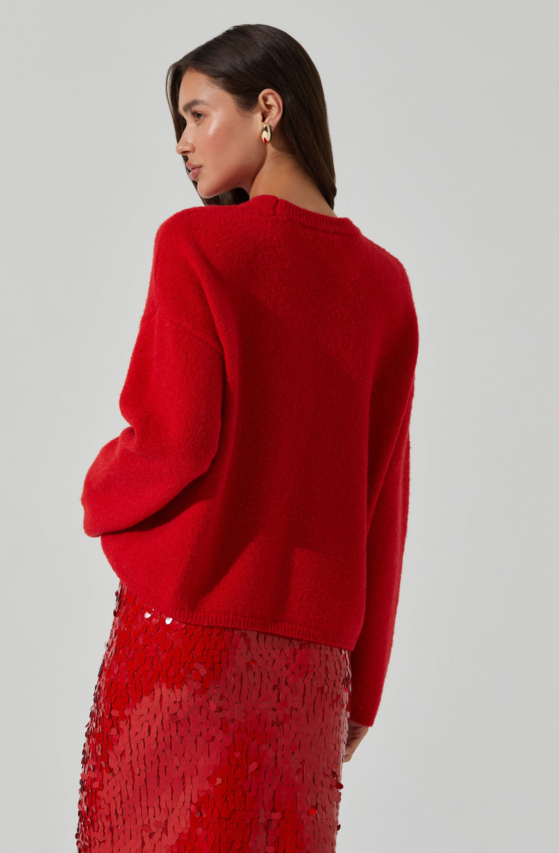 A woman is wearing a bright red, oversized sweater with a soft, fuzzy texture and a round neckline. She is also dressed in a shiny, red, sequined skirt that reflects light, creating a textured, glittering appearance.