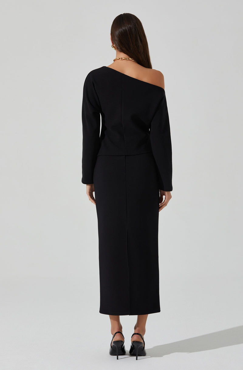 The outfit is a black, long-sleeved dress with an off-the-shoulder design on the left side, exposing the shoulder and collarbone. The dress is fitted at the waist and extends down to the ankles. The wearer is also wearing black high-heeled shoes with an ankle strap.