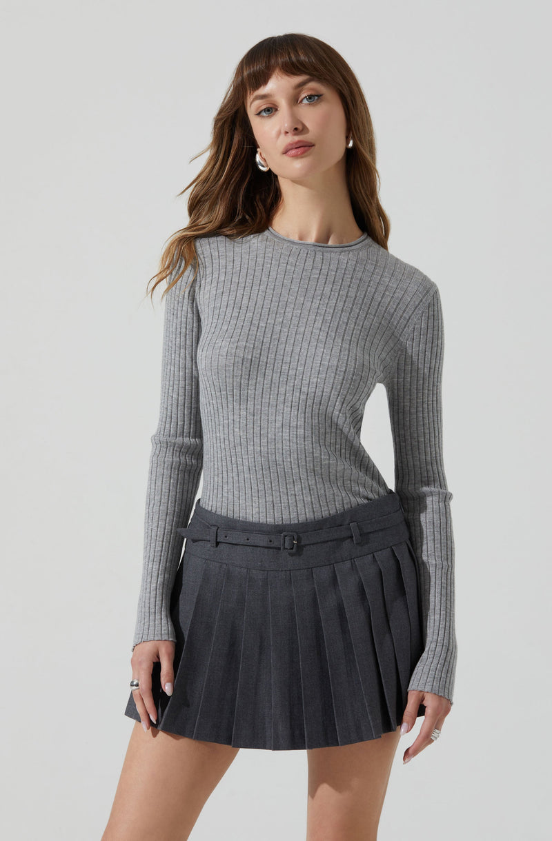 A woman is wearing a fitted, long-sleeve, ribbed sweater in light gray, paired with a dark gray, high-waisted pleated skirt with a matching belt.