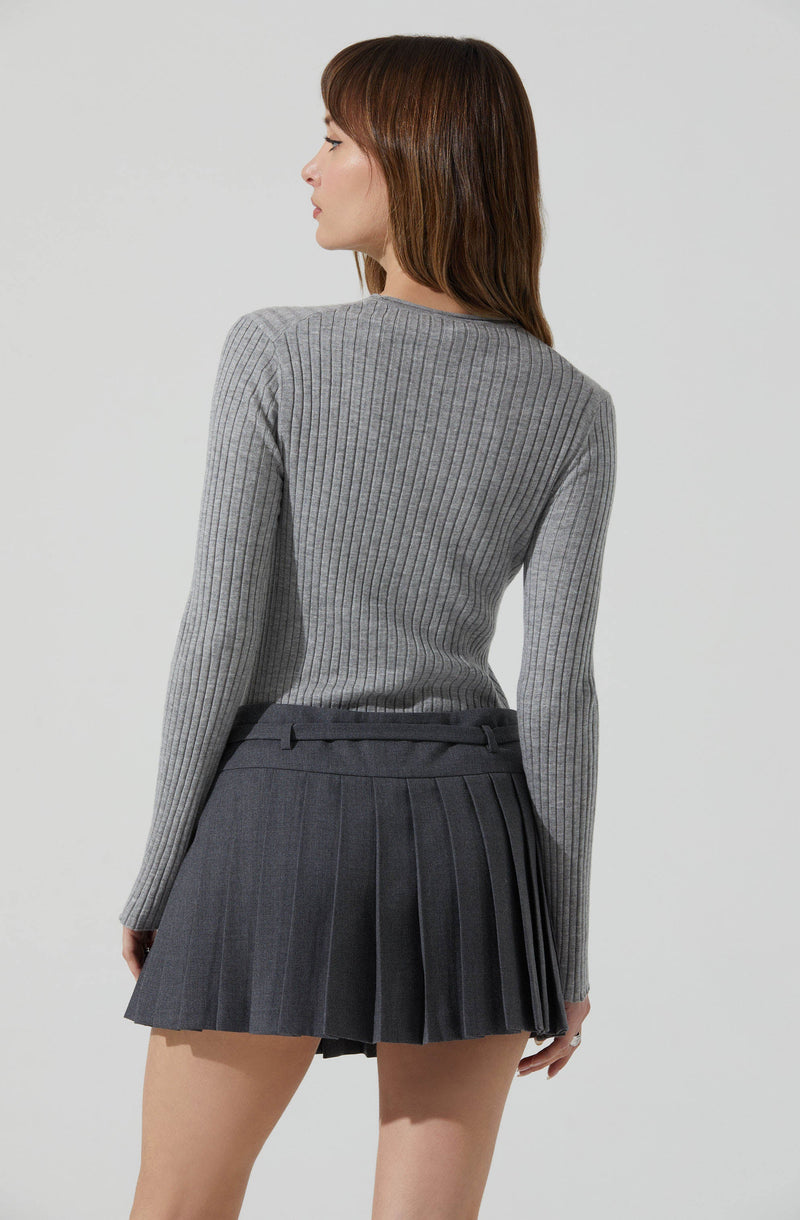 A woman is wearing a fitted, long-sleeve, ribbed, gray sweater with a round neckline, paired with a high-waisted, dark gray pleated mini skirt.