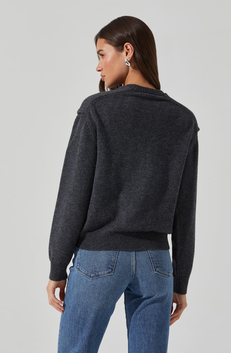 A woman is wearing a dark gray sweater with a ribbed hem and cuffs, and medium wash blue jeans with visible back pocket stitching.