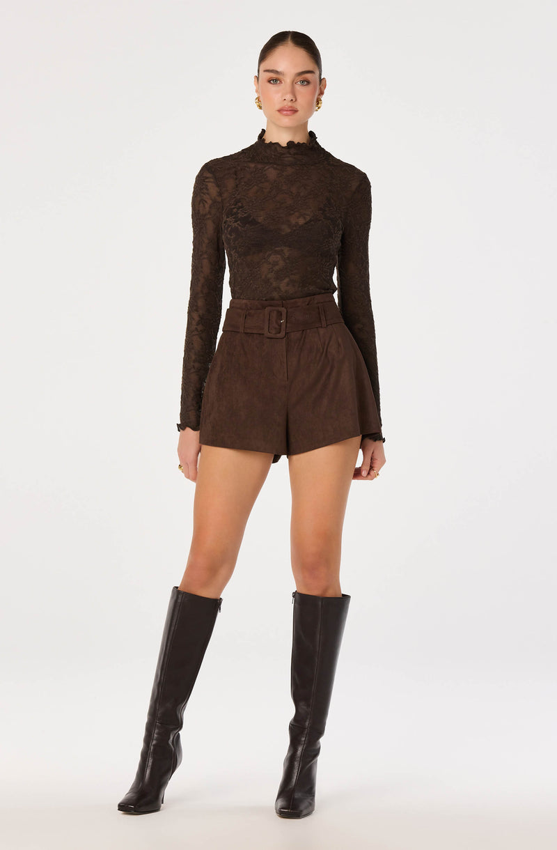 Woman wearing a sheer brown lacy long-sleeve top and matching high-waisted shorts with a belt, black knee-high boots.
