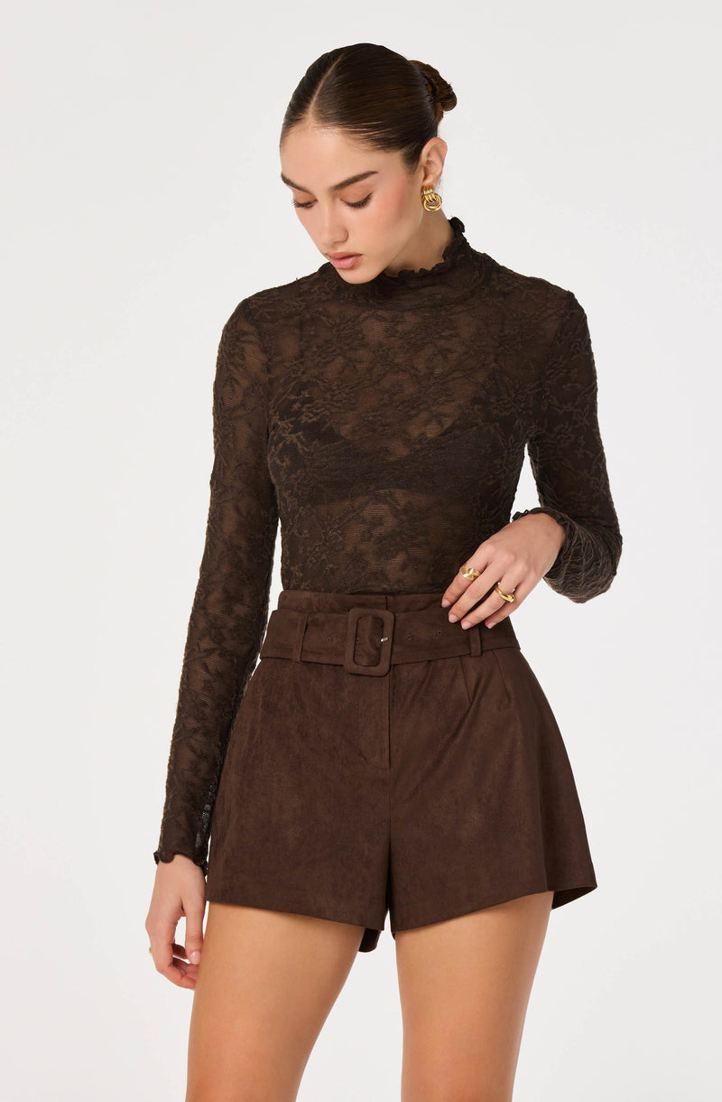 Woman in a black lace long-sleeve top and high-waisted brown shorts with a belt.