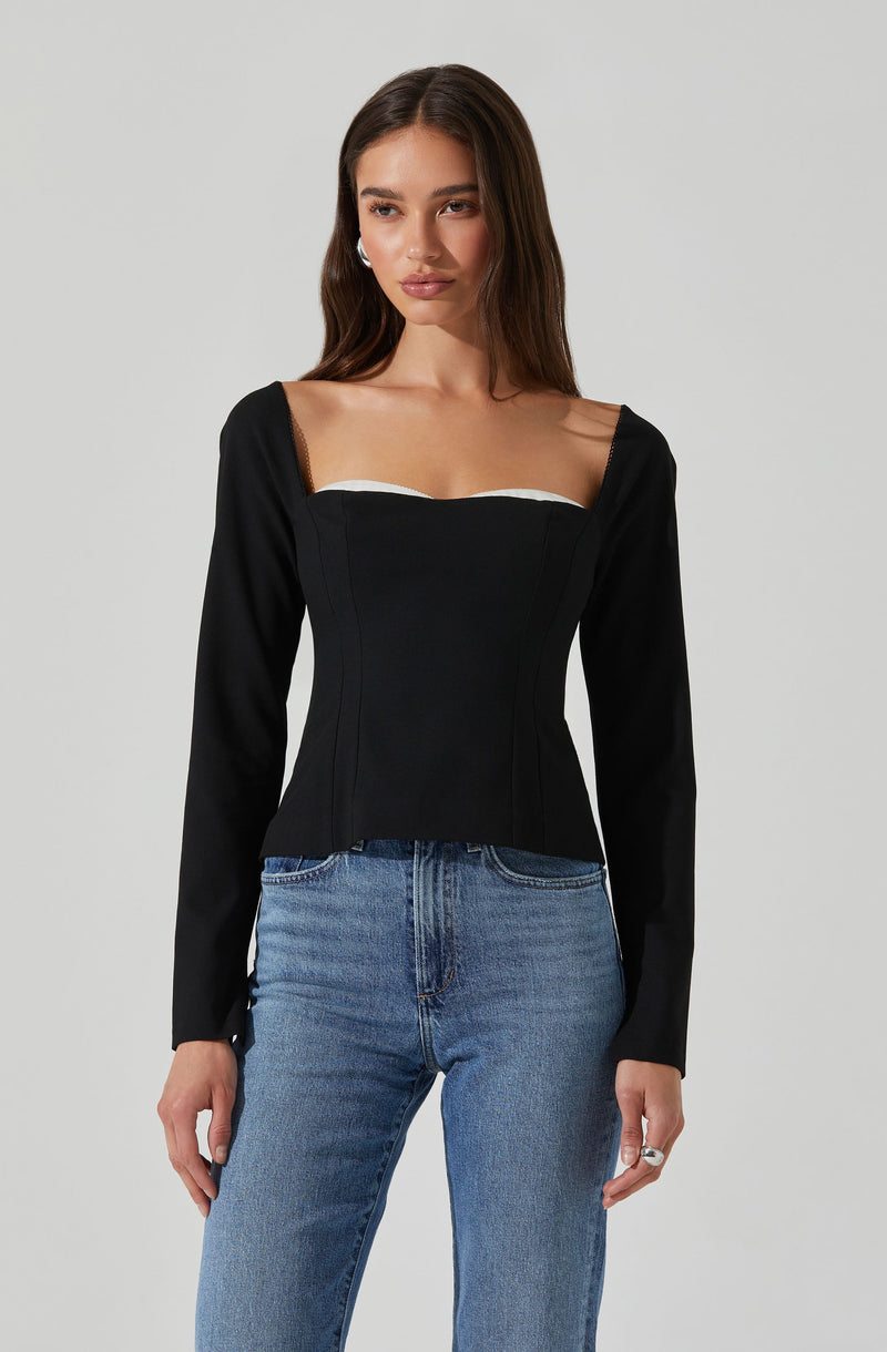 A woman is wearing a fitted black long-sleeve top with a square neckline that has a white trim detail along the top edge. She is also wearing light blue, high-waisted jeans.