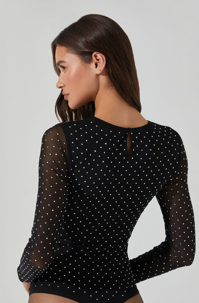 A woman is wearing a black long-sleeve top made of sheer fabric with small white polka dots. The top has a small keyhole opening at the back near the neckline.