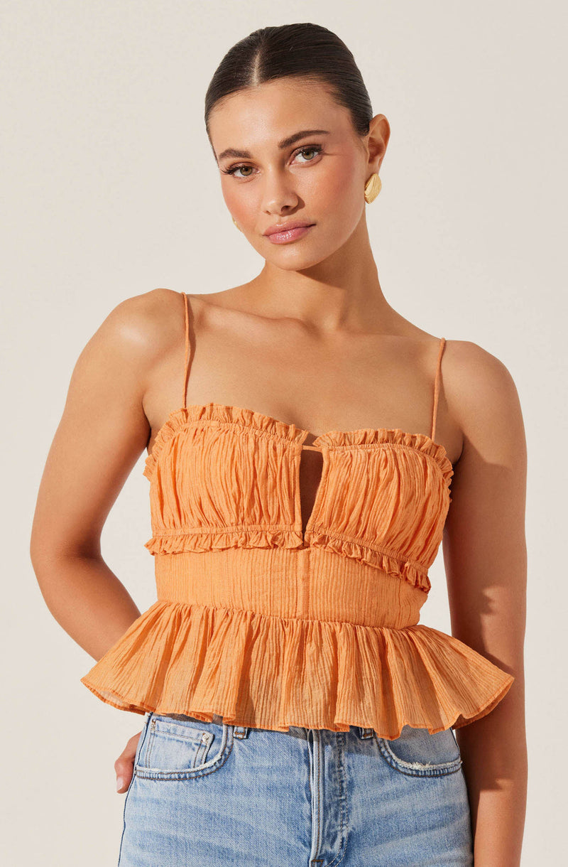 A woman is wearing a sleeveless orange top with thin spaghetti straps. The top features a gathered, ruched fabric with a keyhole opening in the center and a ruffled hem that flares out at the waist. She has paired the top with light blue high-waisted jeans.