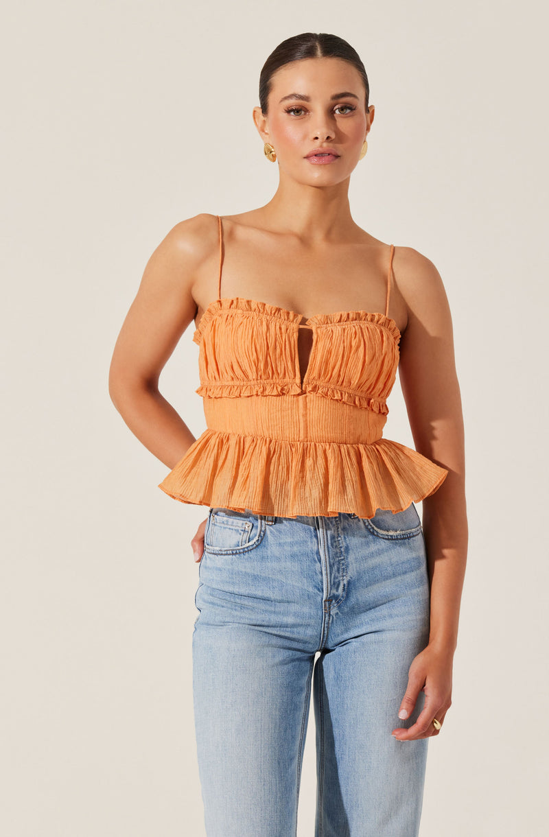 A woman is wearing an orange sleeveless top with thin spaghetti straps. The top features a gathered, crinkled fabric with a keyhole opening in the center of the chest. The waistline is elastic and ruffled, and the bottom of the top has a flared, ruffled peplum design.