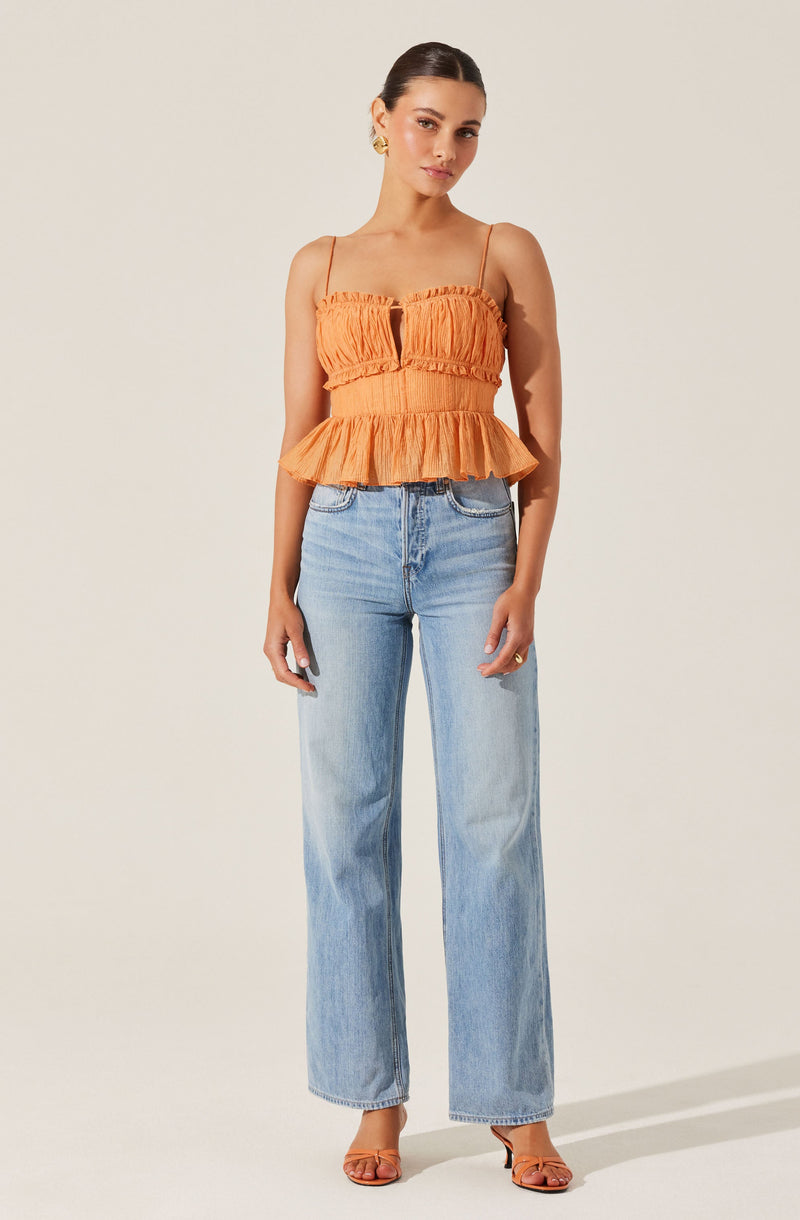 A woman is wearing a sleeveless, orange, ruffled crop top with spaghetti straps and a front keyhole detail. She pairs it with high-waisted, light-wash, wide-leg jeans and tan open-toe heels.