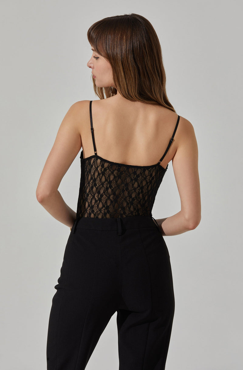 A woman is wearing a black sleeveless top with thin adjustable straps. The top is made of a lace fabric with a floral pattern. She pairs it with high-waisted black pants.