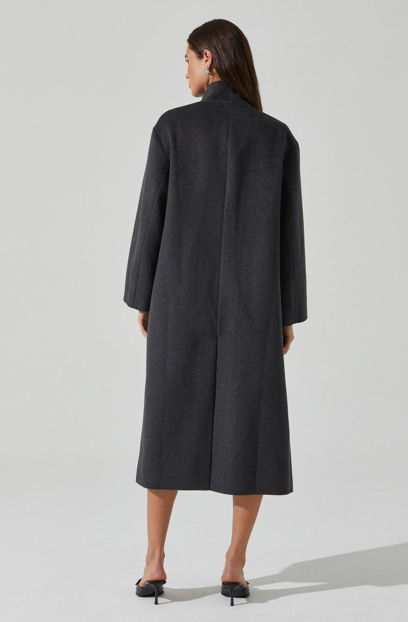 A woman is wearing a long, dark gray, wool coat with a high collar and a center back seam, paired with black high-heeled shoes.