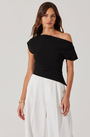 A woman is wearing a black off-the-shoulder top with a loose, draped fit and short, slightly puffed sleeves. She pairs it with high-waisted, wide-leg white trousers that have a pleated detail at the waist.