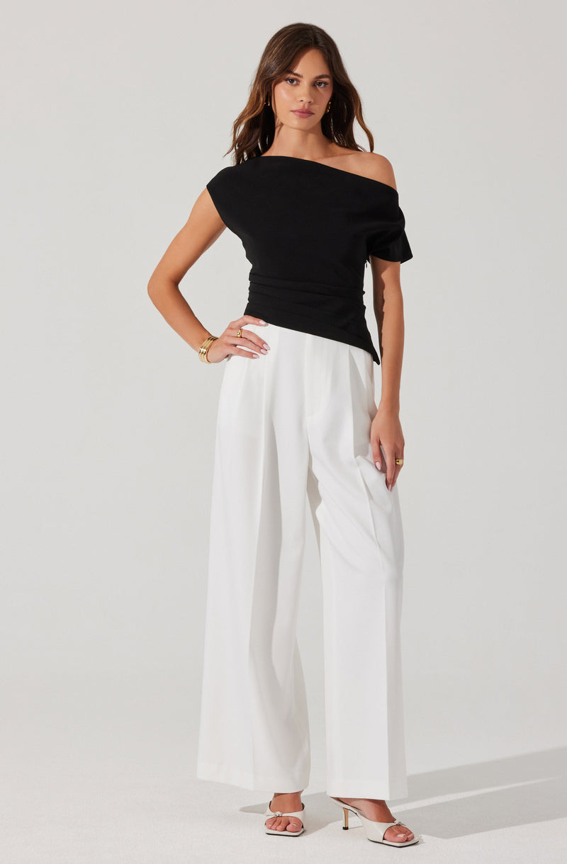 A woman is wearing a black, one-shoulder top with a loose fit and short sleeves, paired with high-waisted, wide-leg white trousers. She is also wearing open-toe, light-colored high heels.
