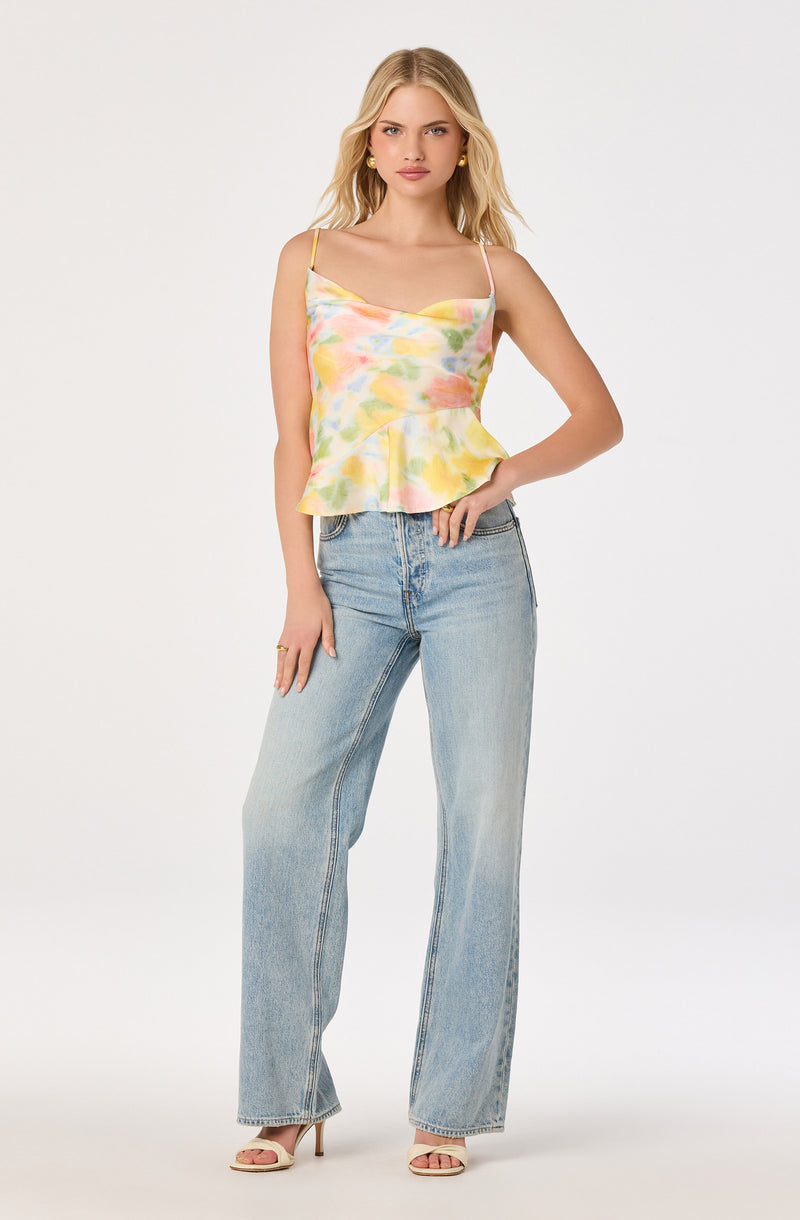 Woman wearing a colorful tie-dye satin camisole with spaghetti straps and light-wash high-waisted jeans.