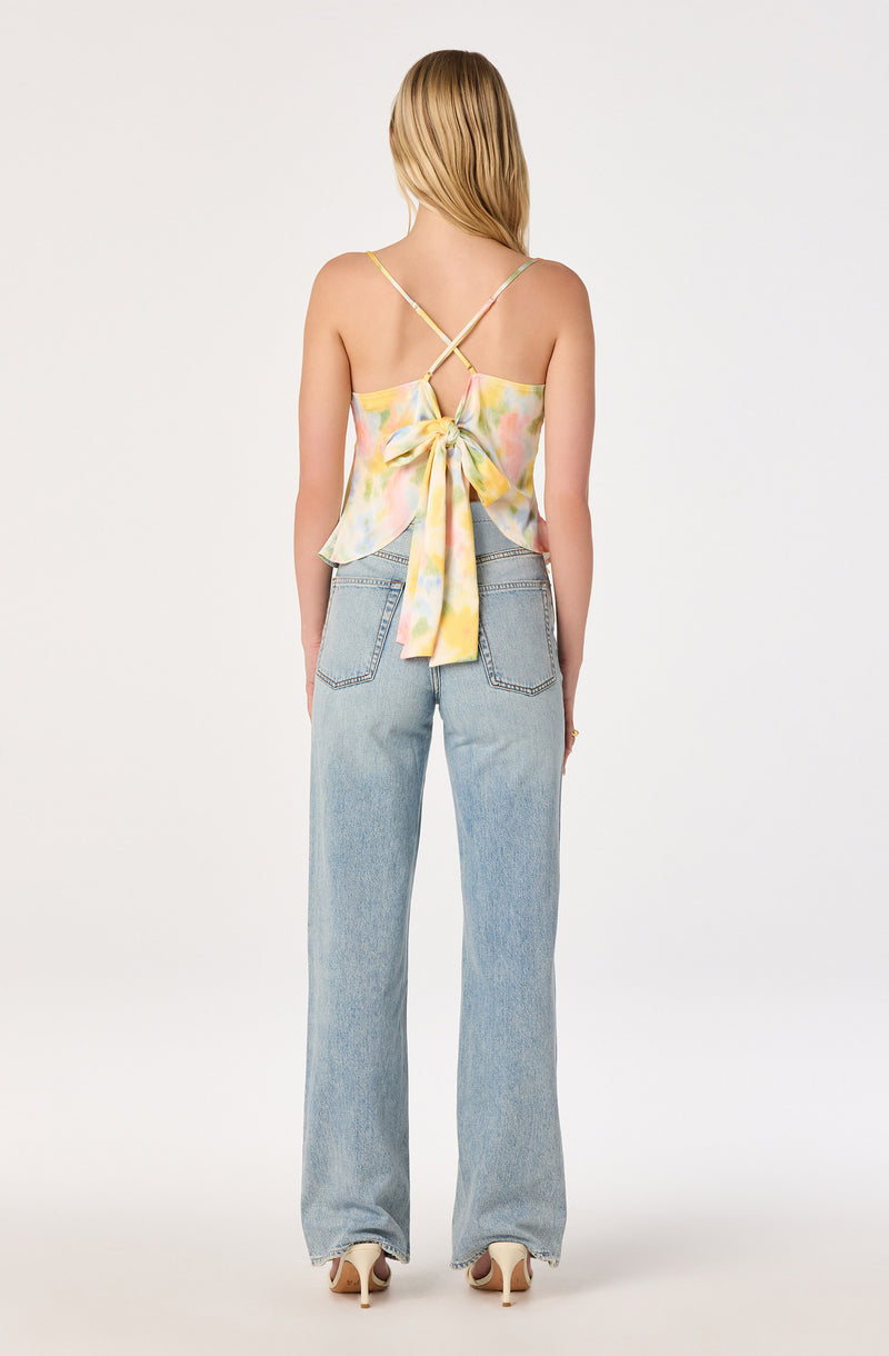 Woman wearing a colorful, pastel tie-dye crop top with thin straps and a large bow in the back.