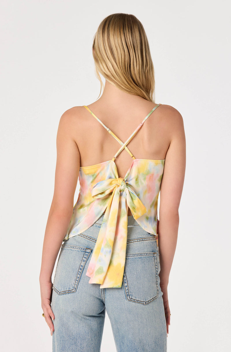 Back view of a woman wearing a sleeveless, pastel-colored, tie-dye top with thin straps crossing at the back and a large bow.