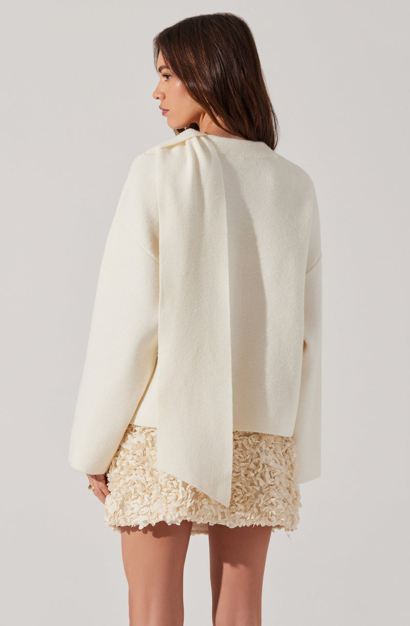 A woman is wearing an oversized, off-white blazer with a relaxed fit and long sleeves. She pairs it with a textured cream-colored skirt that has a floral or ruffled pattern. The overall look is soft and elegant, featuring neutral tones.