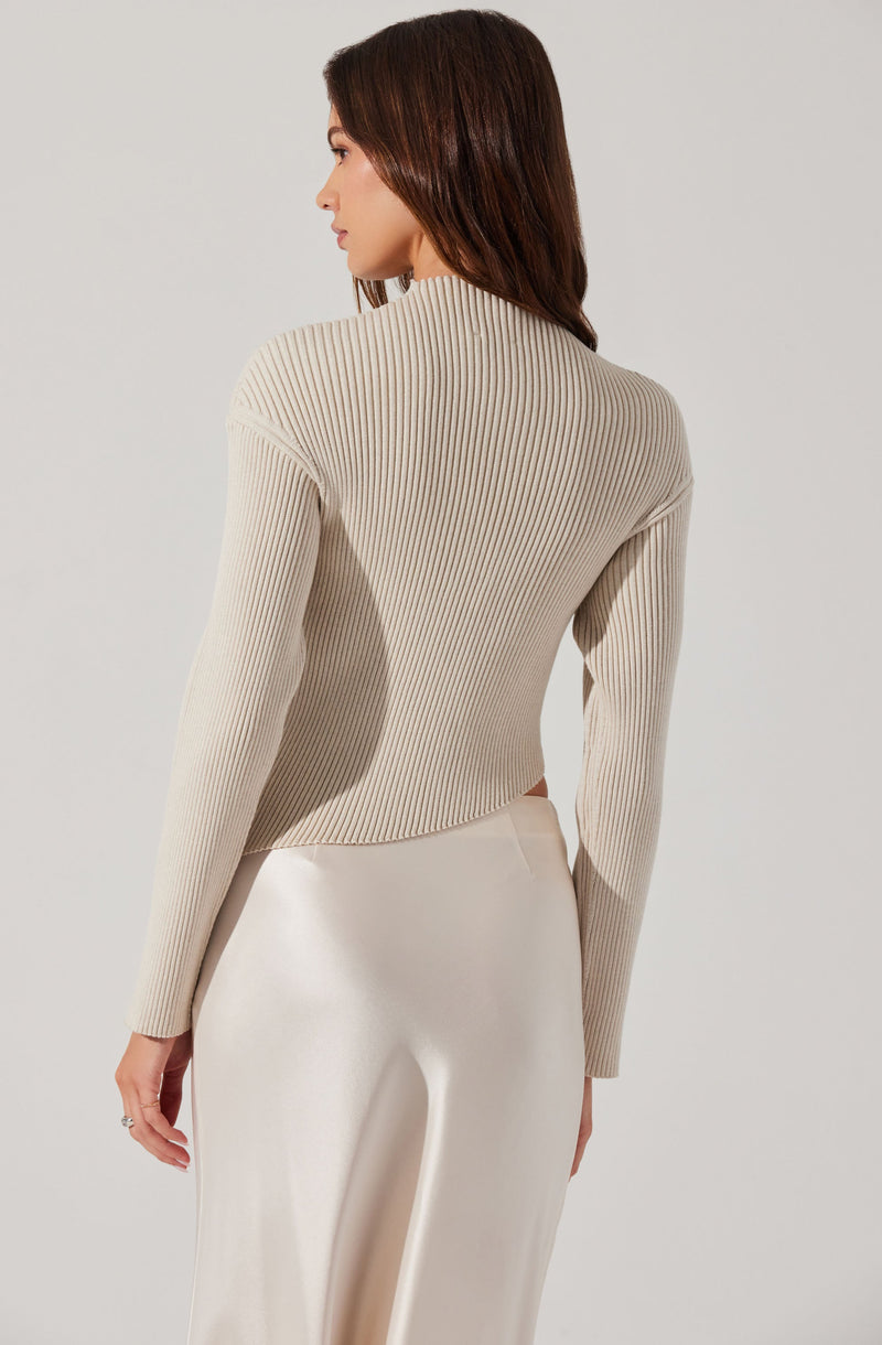 A woman is wearing a beige, ribbed knit sweater with a high neckline and long sleeves. She pairs it with a smooth, satin-like cream-colored skirt.