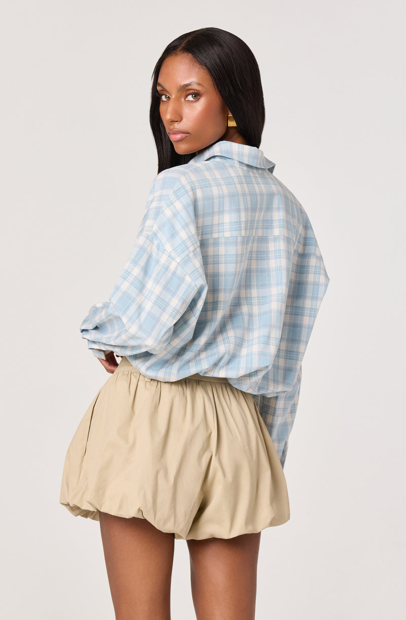 Woman wearing a loose blue plaid shirt and beige puffy shorts.