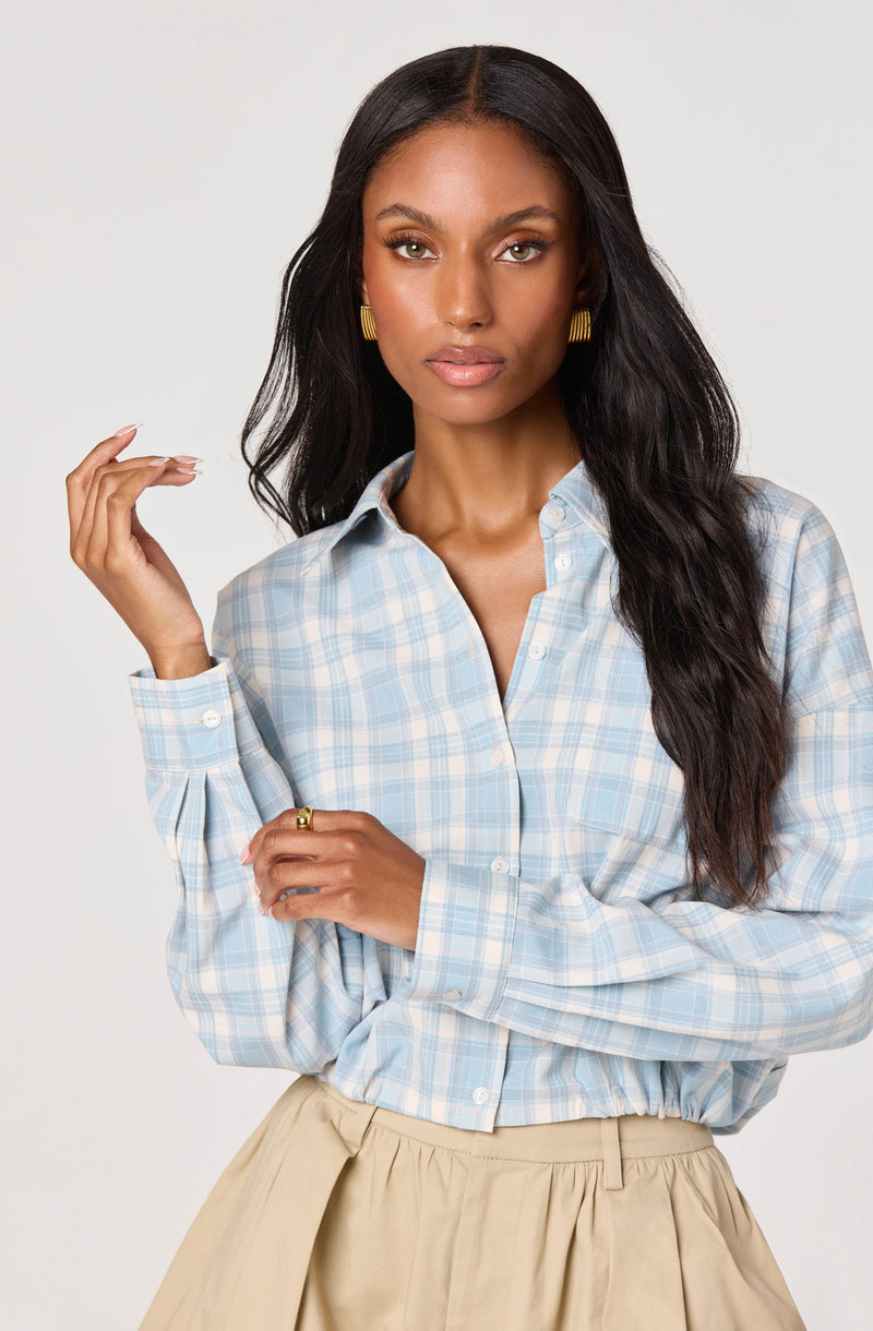 Woman wearing a blue and white checkered button-up shirt and a beige skirt.