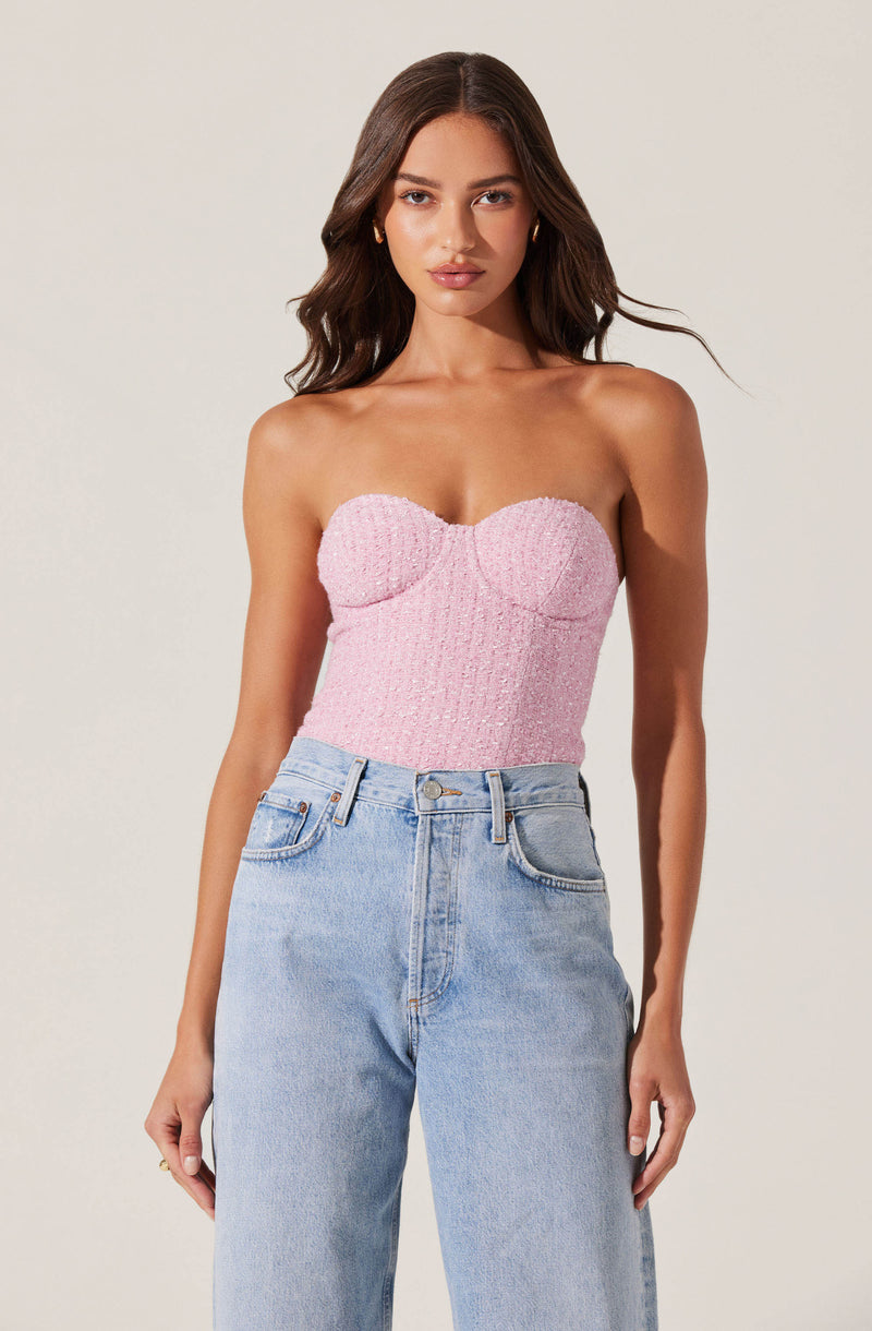 A woman is wearing a strapless pink textured top with a sweetheart neckline. She pairs it with high-waisted, light-wash denim jeans featuring a classic five-pocket design.
