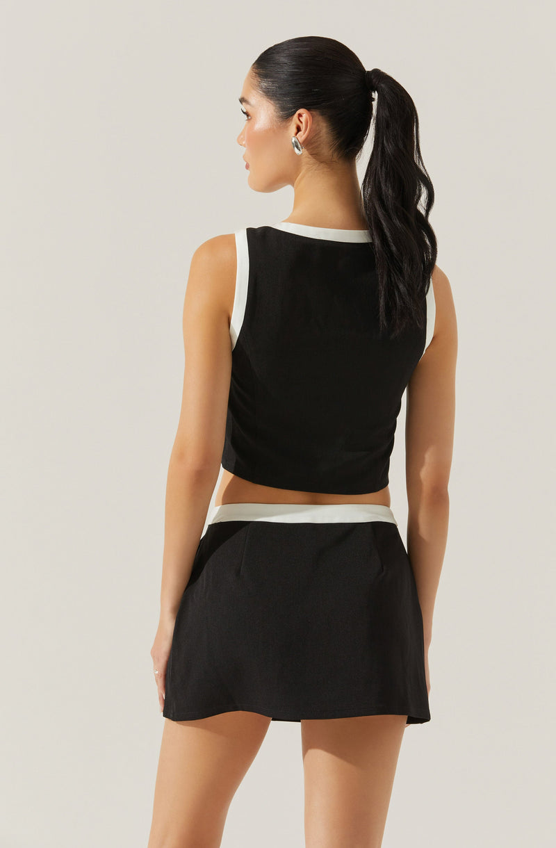 A woman is wearing a sleeveless black crop top with white trim around the armholes and neckline, paired with a matching black skirt that has a white waistband.