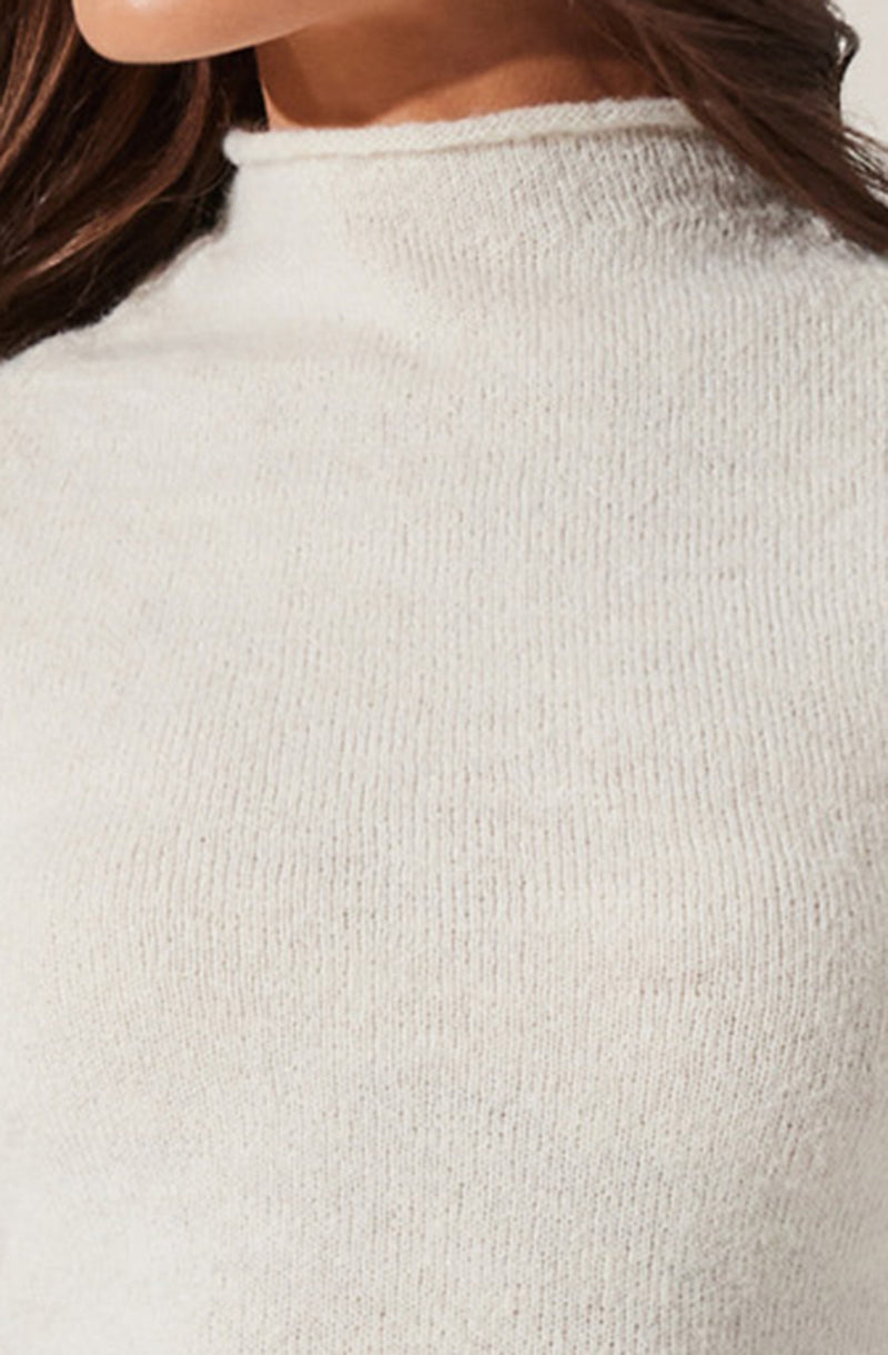 A person wearing a white, long-sleeve, round-neck sweater made of a soft, knitted material. The sweater fits snugly and has a slightly fuzzy texture around the neckline. The person's brown hair is visible on the left side of the image.