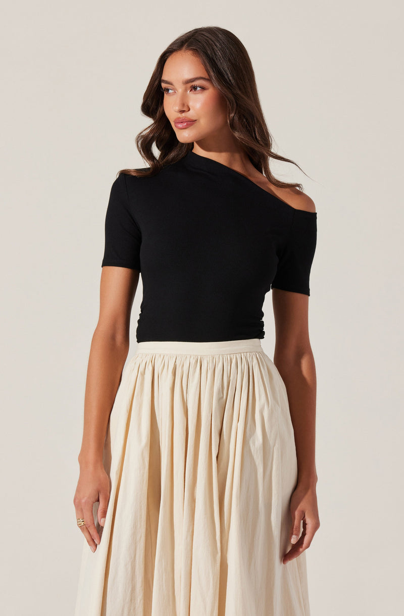 A woman is wearing a black, off-the-shoulder top with short sleeves, paired with a high-waisted, cream-colored, pleated skirt.