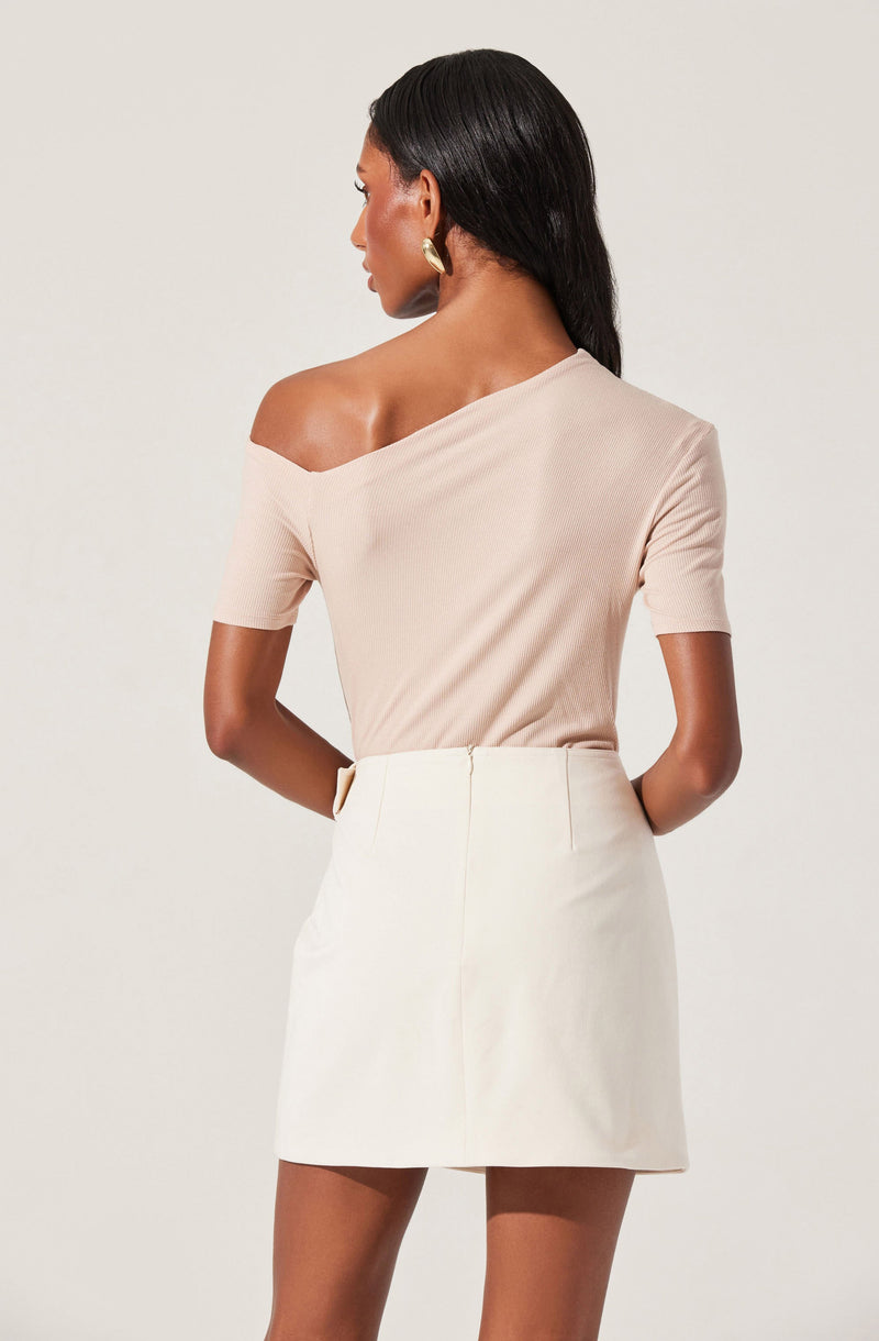 A woman is wearing a beige, off-the-shoulder top with short sleeves, paired with a high-waisted white skirt that reaches mid-thigh.