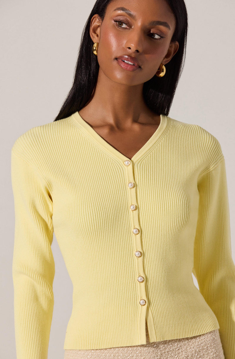 A woman is wearing a light yellow, ribbed, long-sleeve cardigan with a V-neckline. The cardigan has a row of pearl-like buttons down the front.